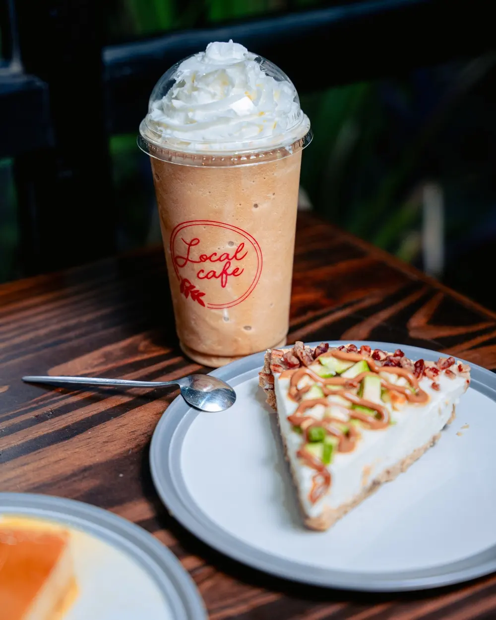 Un frappé con crema batida en el vaso de Local Café, junto a una rebanada de pay