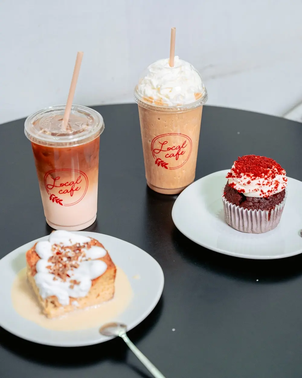 Un café frío, un frappé con crema, un pastel y un cupcake en una mesa de Local Café